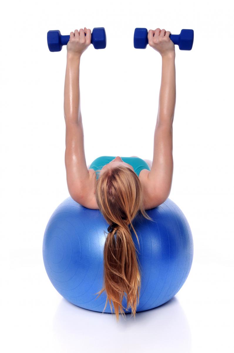 Woman on bouncing ball lifting weights